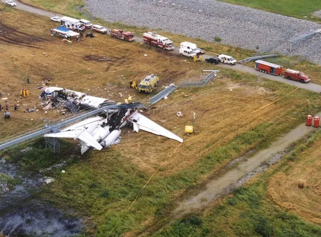 Aerial view of Flight 1420 wreckage beyond the runway, with emergency vehicles alongside.