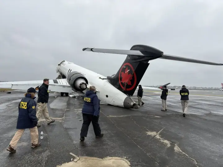 NTSB investigators walking beside damaged aircraft and firefighting vehicle at LaGuardia.