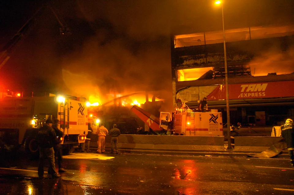 Firefighters and fire engines outside the burning TAM Express building at night.