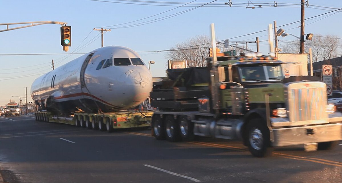 Recovered Flight 1549 fuselage on a low-loader beside a truck on a New Jersey road.